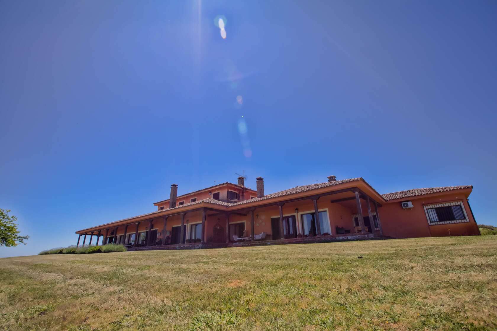 Vista exterior de una casa rural con amplio porche, cielo despejado y césped en primer plano.